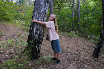 A girl hugs a tree and looks up in the forest