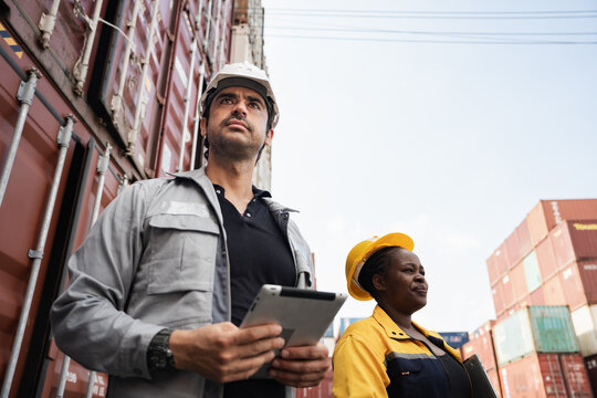 Man and woman logistics workers in high visibility safety gear discuss operations and checking container at shipping container yard	