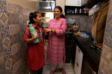 A mother and daughter share a joyful moment as the girl gets ready to leave for school