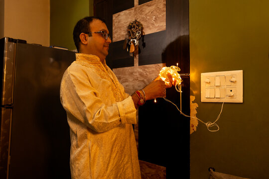 A man checks decorative string lights while preparing the home for a festival