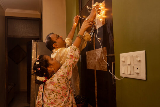 A father and daughter work together to hang decorative string lights during festival preparations