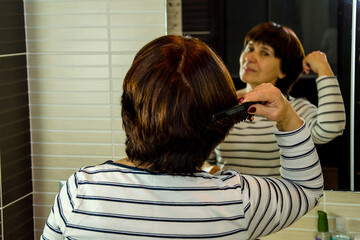 Elderly woman combing hair in bathroom mirror