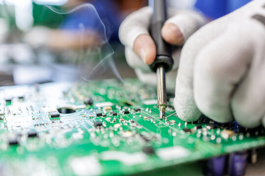 Worker soldering electronic circuit board with soldering iron in electronics factory