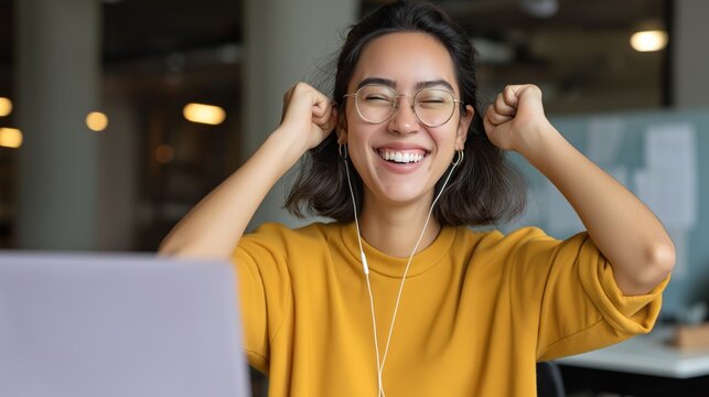 In a bright and inviting office, a cheerful Asian woman expresses joy and excitement as she engages with her laptop. The atmosphere reflects positivity and determination