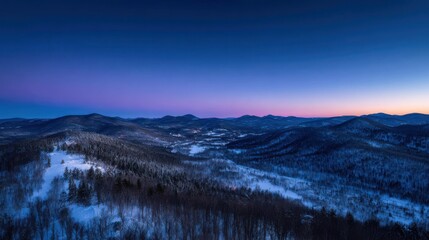 Aerial view of snow covered mountains and forest at twilight with purple and blue sky image