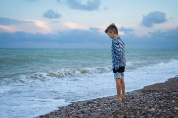 Young boy contemplating waves on pebble beach