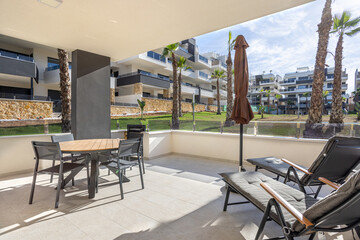 Obraz premium Large sunny terrace with lounge chairs, dining table, and garden view