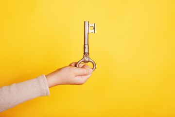 Close-up of a hand holding a vintage brass key against a bright yellow background, symbolizing opportunity and success.