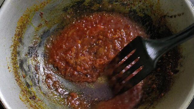 A chef is preparing sambal in a wok. This spicy relish is a commonly served dish essential to Malaysian cuisine.