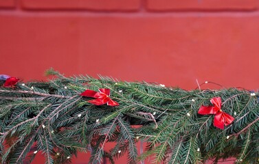 Christmas banner with spruce garland decorated with silk bows on burgundy brick wall background with free space for inserting text