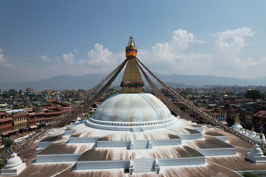 An aerial view of Boudhanath Stupa, Kathmandu, showcasing its majestic dome, colorful prayer flags, and the surrounding city&mdash;a serene Buddhist landmark from above.