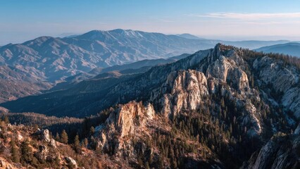 Naklejka premium Snow-dusted jagged peaks rise above pine forests on a rugged ridge, with layered blue mountains fading to the horizon. Concept Snow-dusted Peaks, Pine Forests, Rugged Ridge, Layered Blue Mountains