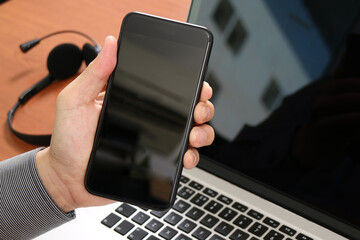 Hand Holding Smartphone with Laptop and Headset on Desk