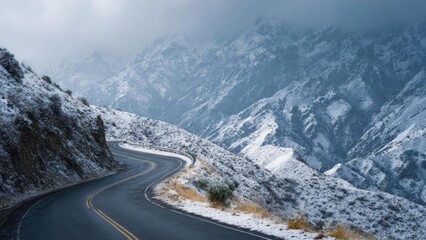 A winding mountain road curving along a snow-covered cliff, with rugged, snow-dusted peaks in the background. Concept Alpine mountain road, Snow-dusted peaks, Rugged cliff scenery