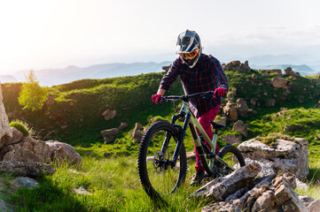 Cyclist in bright clothing climbs a rocky summer trail in clear weather. The concept is extreme sports and enduro, a challenging climb from bicycles up a mountain