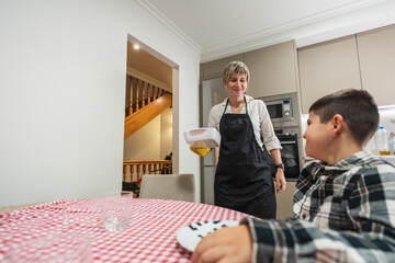 Mother wearing an apron serving food to her son at the dining table. Family enjoying a healthy meal together at home