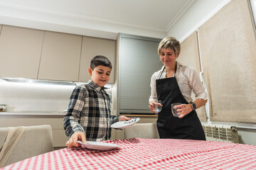 Mother and son smiling while setting the dinner table together. Family bonding during household...