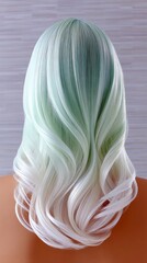 Naklejka premium Back view of a wig or mannequin head displaying long, wavy hair with an ombre effect transitioning from mint green at the top to white at the ends. The hair is