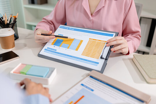 Two female colleagues discussing business reports together in a modern office environment, representing teamwork, data analysis, and collaboration in a start-up company setting.