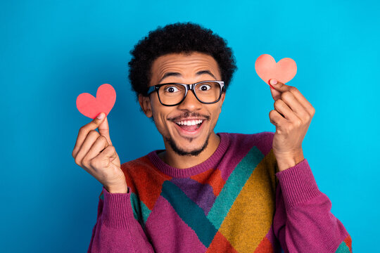 Man holding paper hearts against a blue background showcasing happiness and love in a casual colorful outfit