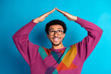 Friendly and stylish young man gesturing with hands against blue background wearing colorful retro sweater and glasses