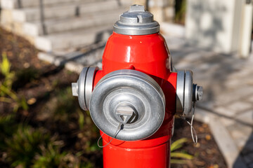 Red outdoor fire hydrant with metal caps in a residential area, photographed in sunlight. Safety...