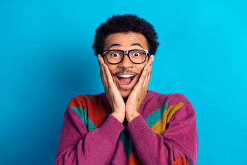 Happy young man wearing stylish sweater expressing surprise against a blue background, showcasing...