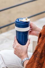 Close-up of a person handing over or receiving a blue travel mug, focusing on the interaction and the product design.
