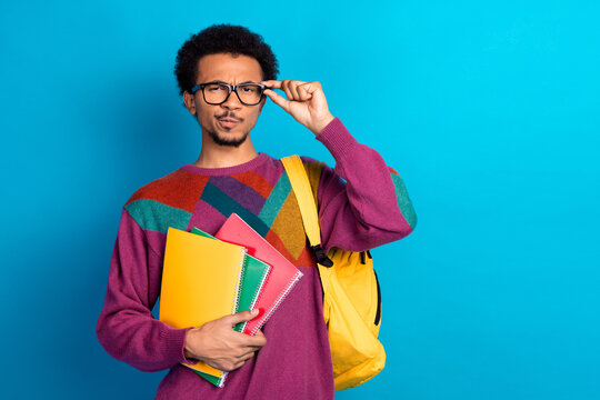 Confident young man with colorful notebook and stylish sweater expressing curiosity against a vibrant blue background