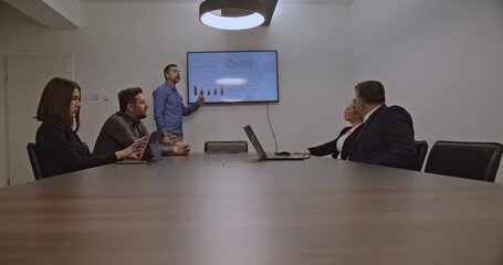 Businesspeople in a meeting discuss charts and data displayed on a monitor. A diverse team collaborates on a project in a modern office. - Powered by Adobe