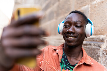 Young African man smiling, wearing headphones and capturing a selfie on phone