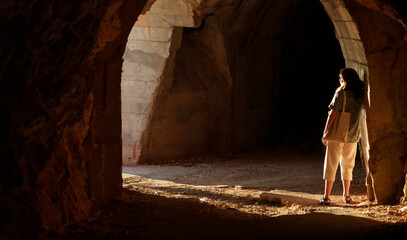 A girl poses in a tunnel, the beautiful sunset sunlight creates long shadows on the arch and walls