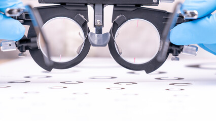 An optometrist wearing blue gloves measures visual acuity using special test glasses for lens selection. High quality photo