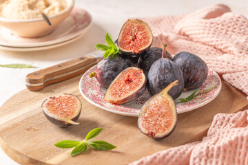 Sliced and whole figs on a plate and a wooden board with a knife, a pink napkin, and a bowl of crumble in a rustic setting