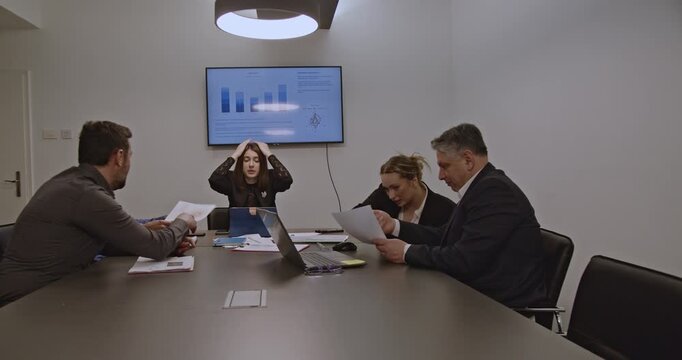 Businesspeople discuss company strategy and analyze data charts in a meeting room. Stressful atmosphere, urgent decisions, and collaborative problem-solving.