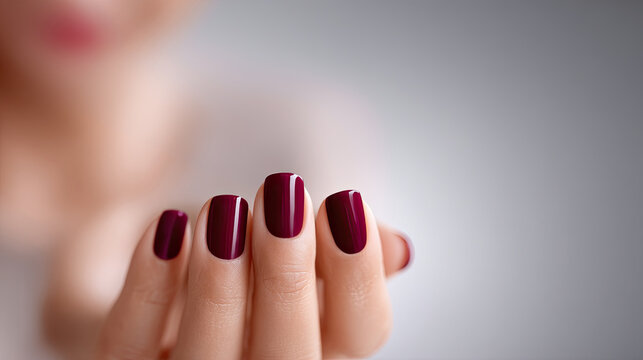 Close-up of a woman applying deep burgundy nail polish, showcasing meticulous attention to detail and elegance in personal grooming
