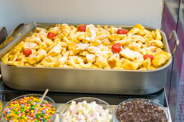 traditional austrian kaiserschmarrn dessert, shredded pancake topped with powdered sugar and garnished with strawberries, served in a metal tray with toppings bar below, concept of bakery