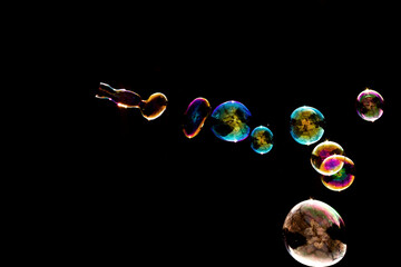 Flowing Diagonal Line of Colorful Soap Bubbles with Gold, Pink, Blue, and Rainbow Iridescence on Black Background - Abstract Bubble Stream Photography Showing Dynamic Movement and Light Reflection

