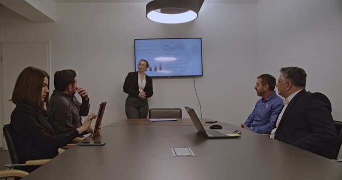 Business team in a meeting room, discussing financial data displayed on a monitor during a productive office workday.