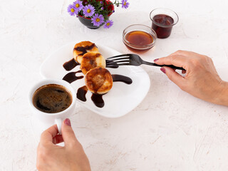 Woman with curd fritters on the porcelain plate and a cup of coffee.