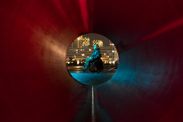 Pondering disabled young man in wheelchair sitting alone outdoors in neon rgb light, enjoying fresh air, engaged in deep thinking, reflecting on thoughts and feelings, relieving daily stress outside.