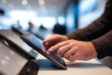 A customer examines a tablet in a modern electronics store. Close-up of a man's hand touching the screen. In-store technology demonstration and shopping experience