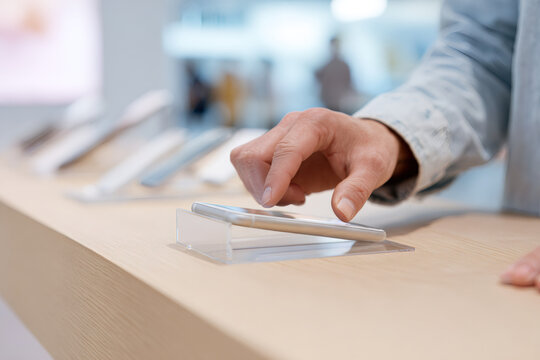 A customer examines a new smartphone on display in a store. Close-up of a hand touching the screen while shopping for electronics. Technology sale and consumer choice concept