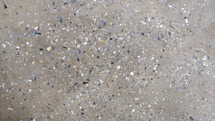 A close-up view of a textured concrete surface with embedded aggregate stones and pebbles.