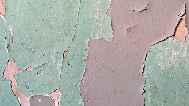 Close-up of weathered green and brown paint peeling off a textured wall surface, showing signs of decay and age.
