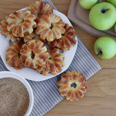 Homemade puff pastry apple rings with cinnamon and cane sugar on white ceramic plate on wooden table with fresh apples