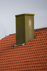 Naklejka premium A rectangular chimney rises from a red-tiled sloped roof, surrounded by metal flashing and weathered textures.
