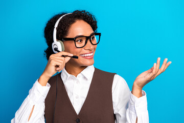 Young female worker with headset and glasses presenting friendly professional service in bright blue studio background