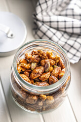 Nuts coated in sugar glaze in jar on white table.