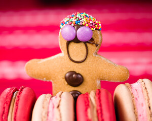 A gingerbread man with chocolate buttons is surrounded by red and cream-colored macarons.